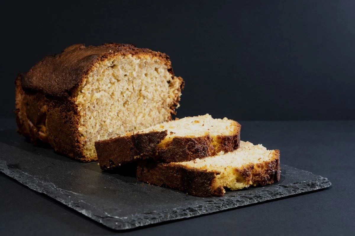 Bananenbrood met een gesneden plak op een leisteen plankje tegen een donkere achtergrond