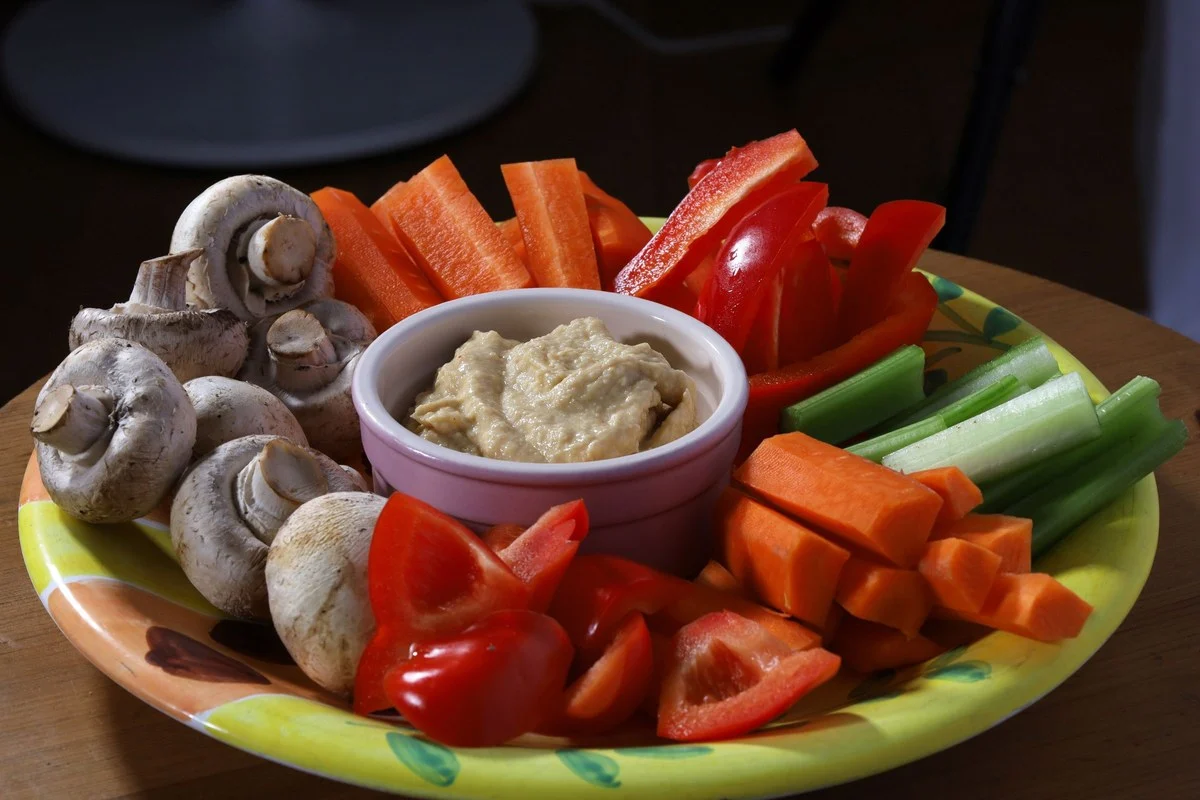 Schaal met reepjes paprika, wortel, champignons en lente-ui rond een bakje hummus