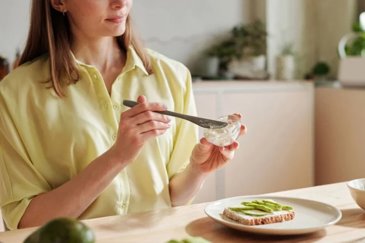 Vrouw smeert toast met avocado in een lichte keuken; hoeveel calorieën per dag vrouwen nodig hebben verschilt