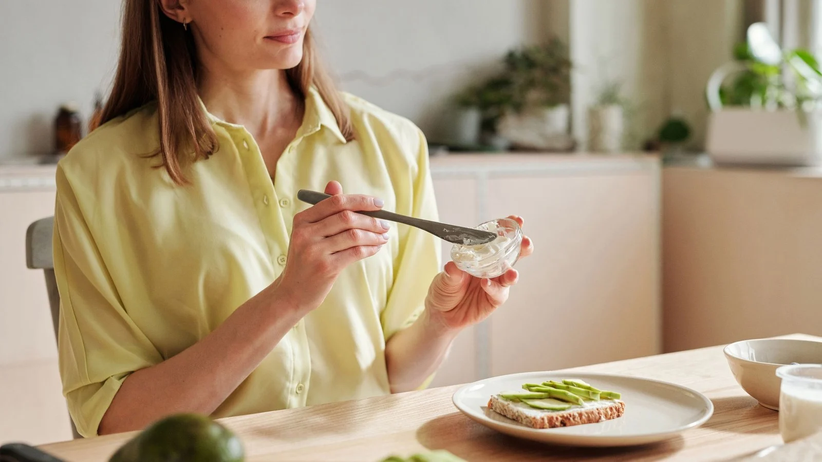 Vrouw smeert toast met avocado in een lichte keuken; hoeveel calorieën per dag vrouwen nodig hebben verschilt