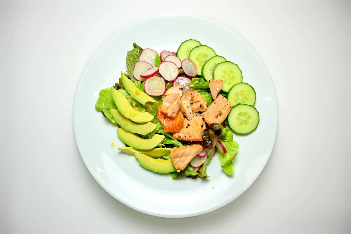 Wit bord met salade van zalm, plakjes avocado, komkommer en radijs, een maaltijd die past bij een keto dieet