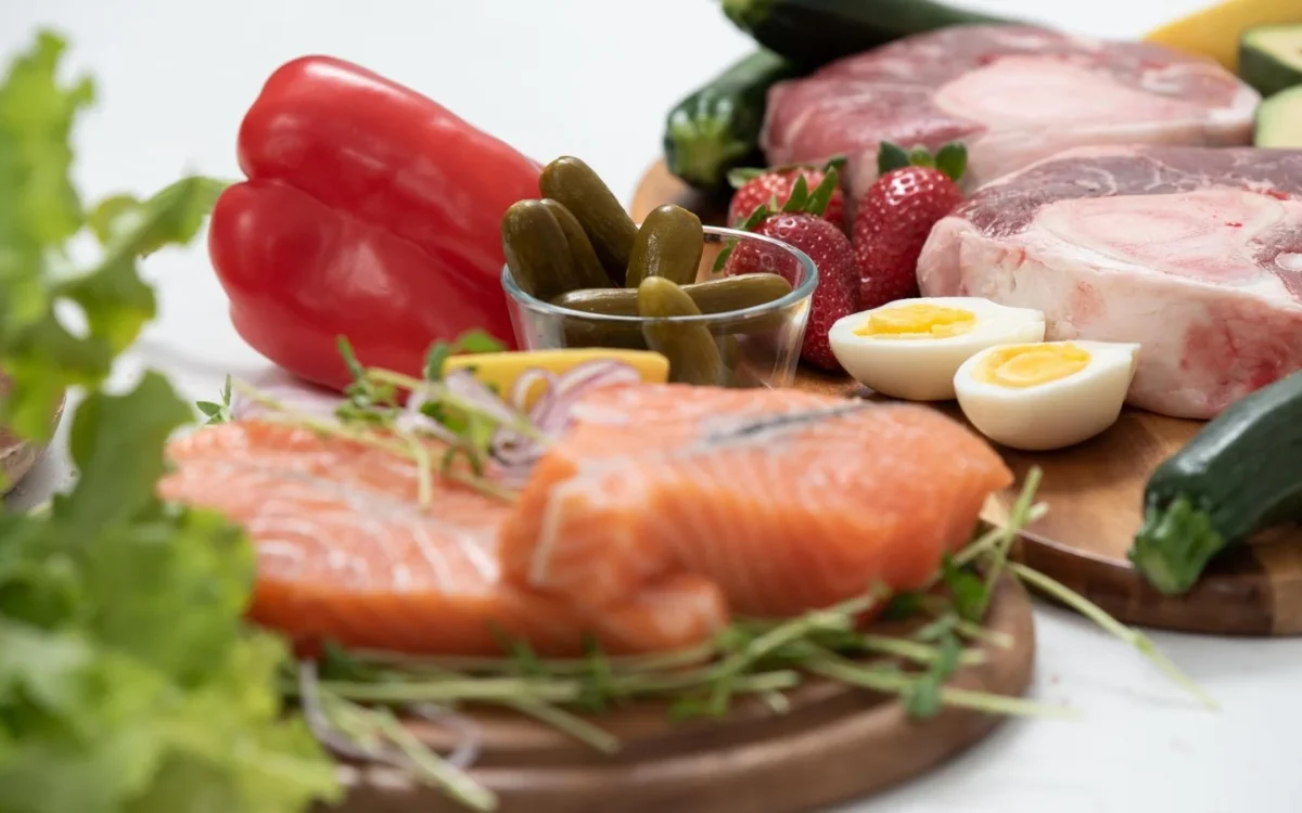 Ketoproducten op houten planken: zalm, rauw vlees, gekookte eieren, paprika, augurk en sla