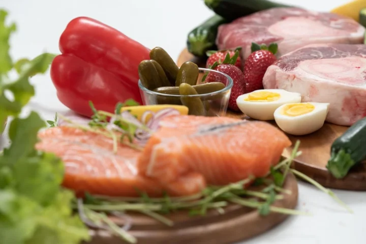 Ketoproducten op houten planken: zalm, rauw vlees, gekookte eieren, paprika, augurk en sla