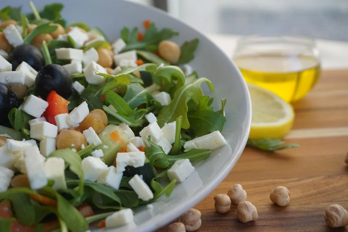 Salade met feta, olijven, kikkererwten en rucola met een kannetje olijfolie op de achtergrond