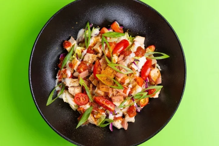 Salade met kip, tomaat en lente-ui in een zwarte kom