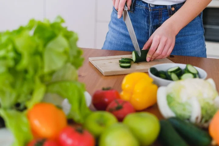 Verse groente en fruit op het aanrecht terwijl iemand komkommer snijdt: snel afvallen begint in de keuken