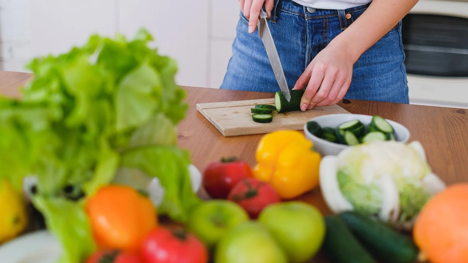 Verse groente en fruit op het aanrecht terwijl iemand komkommer snijdt: snel afvallen begint in de keuken