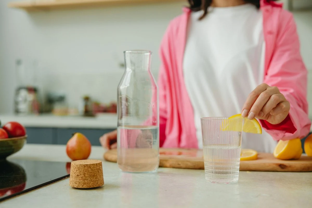 Vrouw in een lichte keuken doet een schijfje citroen in een glas water