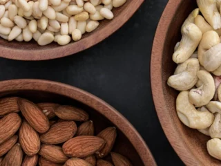 Amandelen, cashewnoten en pijnboompitten in houten schalen; waar zit magnesium in? Onder meer in noten
