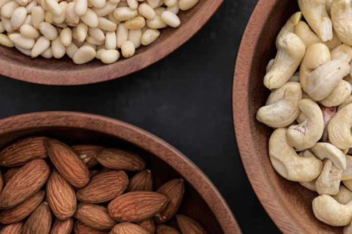 Amandelen, cashewnoten en pijnboompitten in houten schalen; waar zit magnesium in? Onder meer in noten