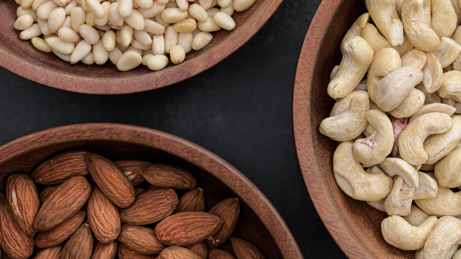 Amandelen, cashewnoten en pijnboompitten in houten schalen; waar zit magnesium in? Onder meer in noten